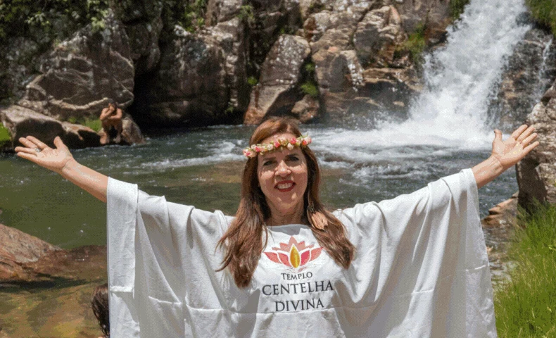 Michelle Maria Frota Ximenes de braços abertos diante de uma cachoeira na Chapada dos Veadeiros